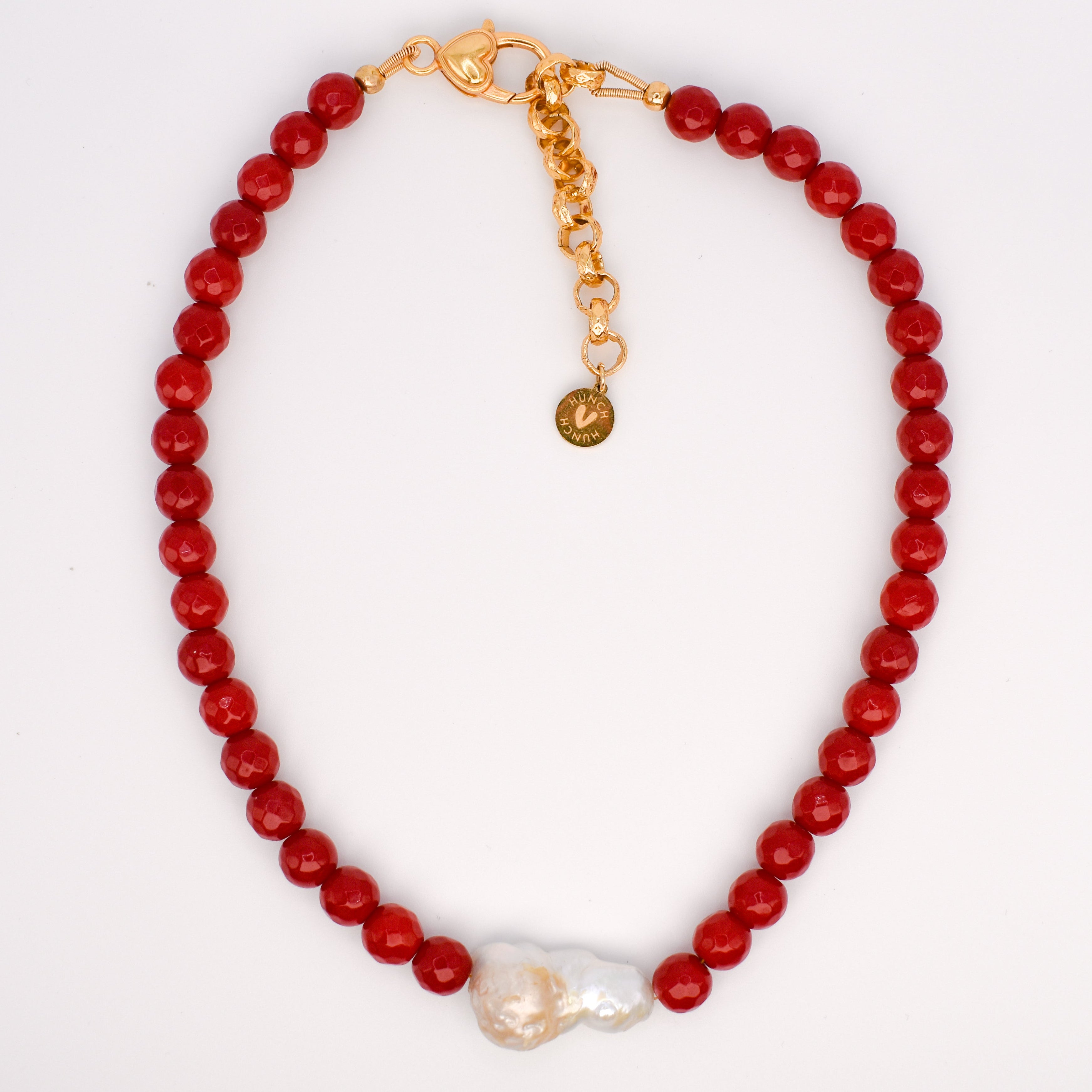 A red beaded necklace with a gold clasp and extender chain, featuring a white baroque pearl accent at the bottom center, displayed on a white background.