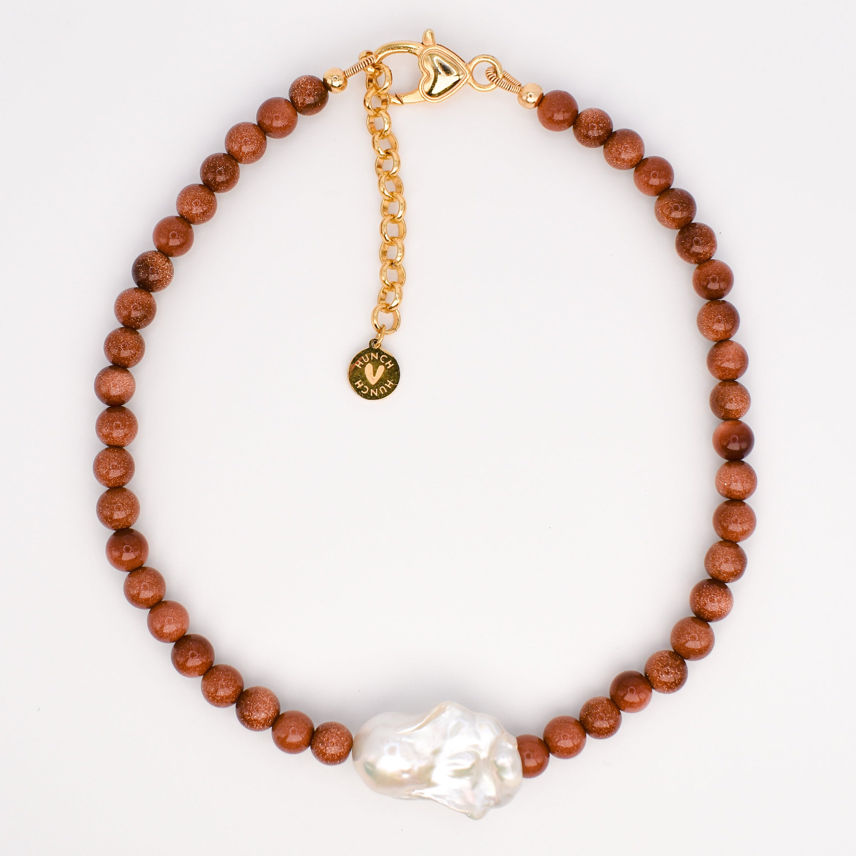 A beaded bracelet with round sand stone  beads, gold plated 24 k  chain extender with a small round charm, and a large white baroque pearl  at the front, displayed on a white background.