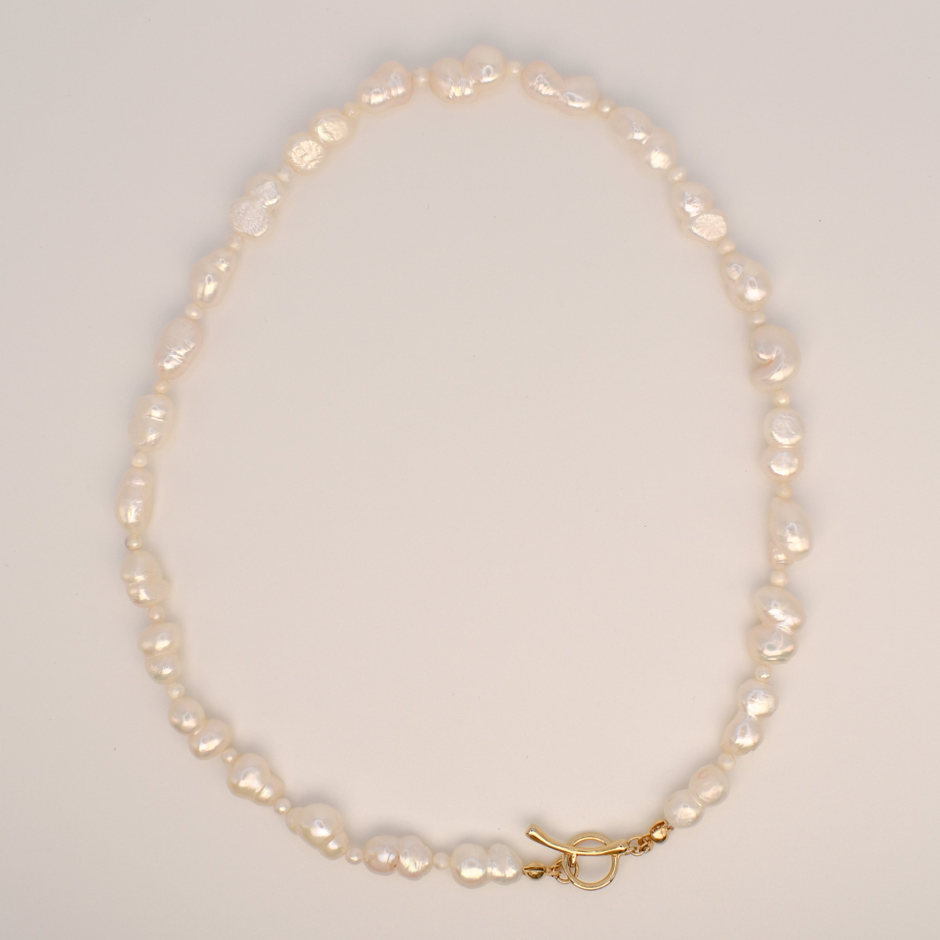 A single-strand baroque pearl necklace with a gold  toggle clasp, displayed on a white jewelry card.
